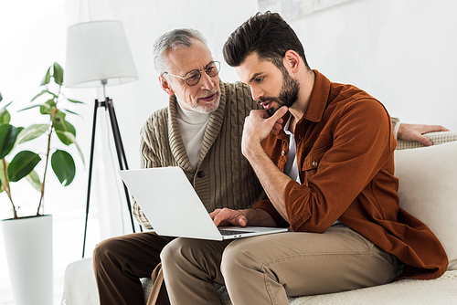 senior father looking at handsome son sitting with laptop