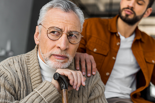 cropped view of son putting hand on shoulder of upset senior father in glasses