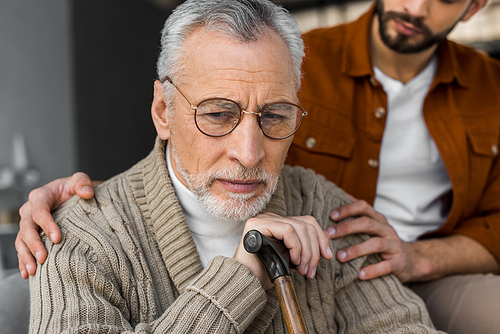 cropped view of son putting hands on shoulders of upset senior father in glasses