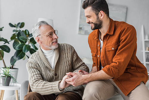 happy senior father in glasses holding hands with handsome son at home