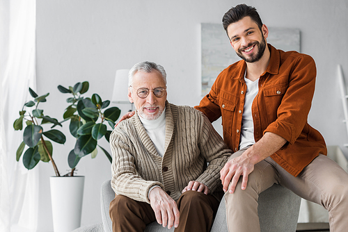 happy senior father in glasses sitting near handsome and cheerful son at home