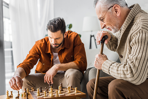 selective focus of senior father in glasses playing chess with son