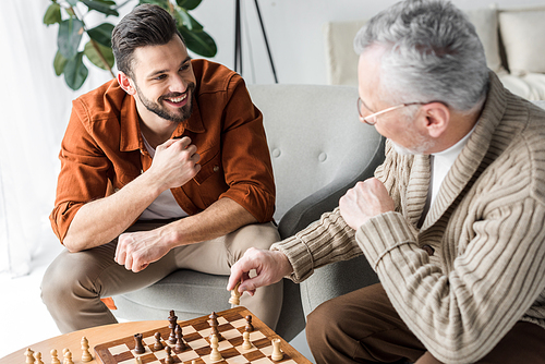 retired father in glasses looking at happy son while playing chess