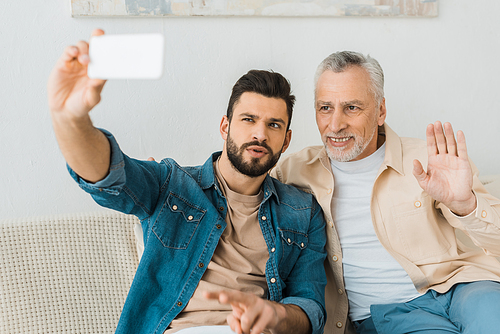 handsome bearded man taking selfie with senior father at home