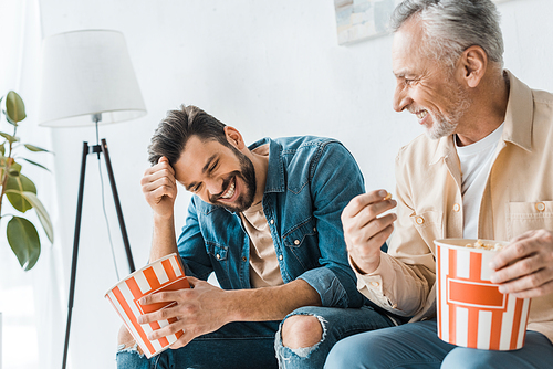 happy senior father sitting with smiling son and holding popcorn bucket