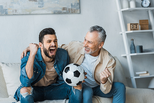 senior man looking at happy son cheering while watching championship and holding football