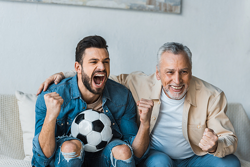 happy senior man watching championship and cheering with handsome son holding football