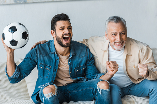 senior man watching championship and cheering with handsome son holding football