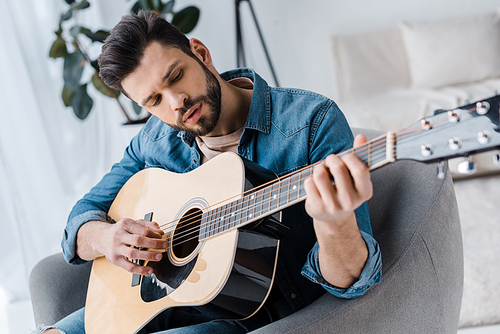 handsome bearded man playing acoustic guitar at home