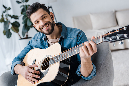 cheerful bearded man playing acoustic guitar at home