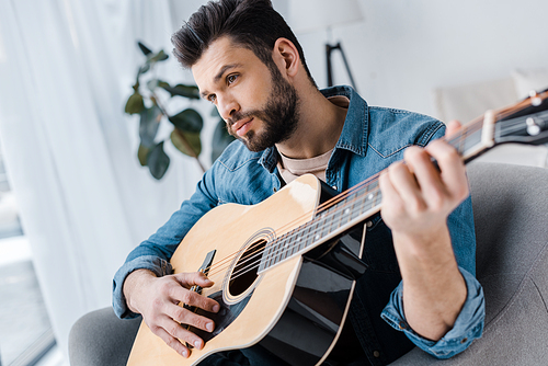 bearded and handsome man playing acoustic guitar at home