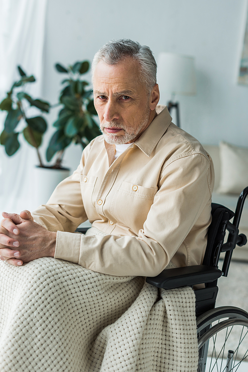 sad disabled retired man sitting in wheelchair with clenched hands and