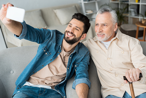 cheerful son taking selfie with retired cheerful father on smartphone