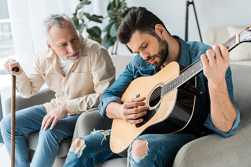 handsome bearded man playing acoustic guitar near happy senior father at home