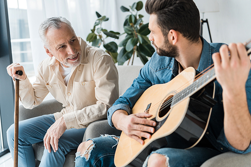bearded son playing acoustic guitar near happy senior father at home