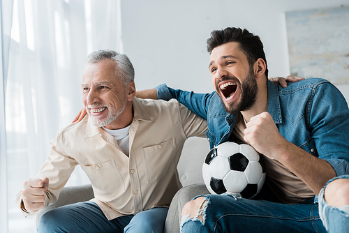 happy retired man watching championship and cheering with handsome son holding football