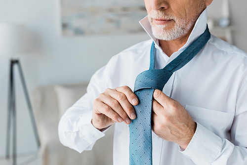 cropped view of confident and elegant senior man tying tie at home