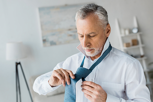 confident and elegant retired man tying blue tie at home