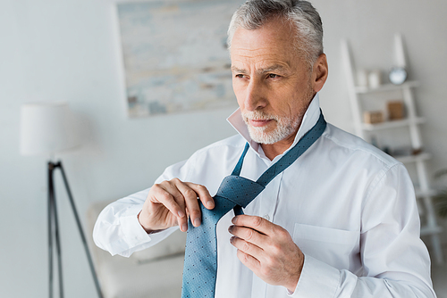 elegant and confident retired man tying blue tie at home