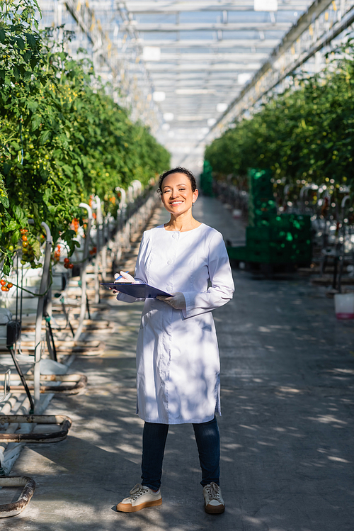 happy african american quality inspector standing with clipboard in greenhouse