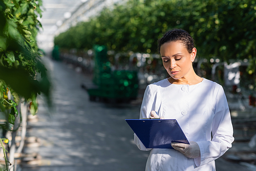 african american agricultural technologist writing on clipboard in greenhouse