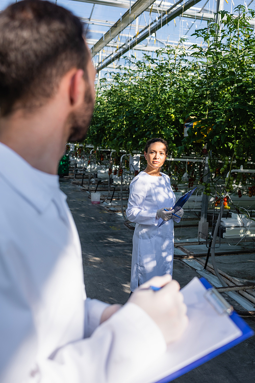 african american quality inspector looking at colleague with clipboard on blurred foreground