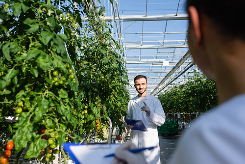 quality inspector pointing with finger in greenhouse near african american colleague on blurred foreground