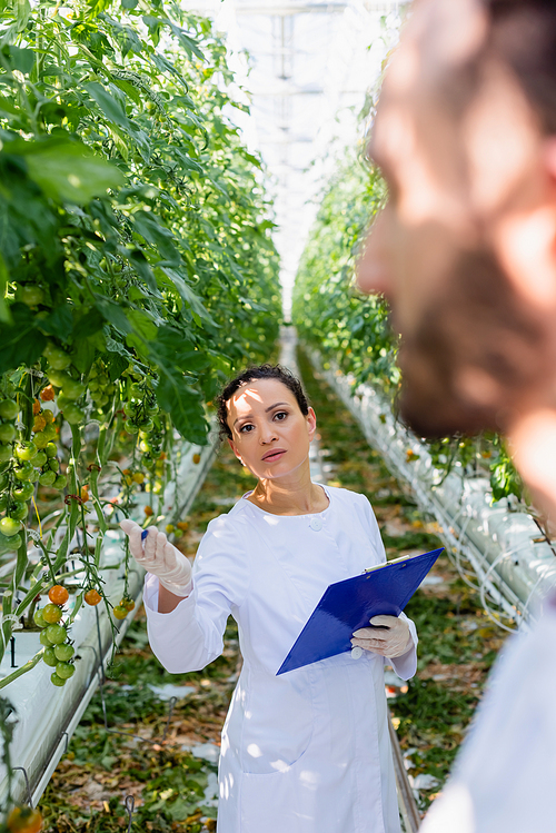 african american quality inspector pointing with hand near colleague on blurred foreground