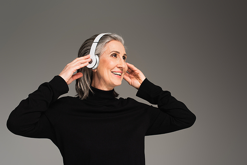 Cheerful woman using headphones isolated on grey