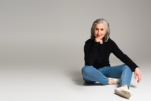 Smiling grey haired woman smiling while sitting on grey background