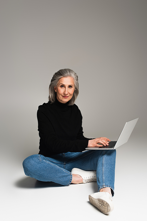 Mature woman using laptop and  on grey background