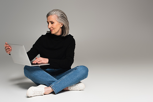 Grey haired woman using laptop on grey background