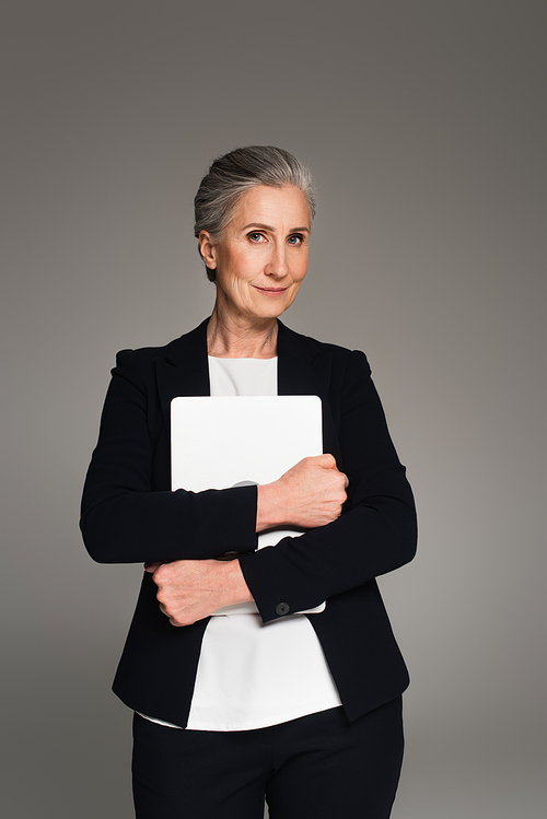 Mature woman in formal wear holding laptop isolated on grey