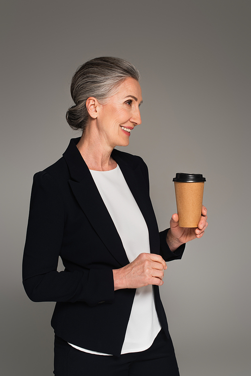 Cheerful businesswoman in formal wear holding takeaway drink isolated on grey