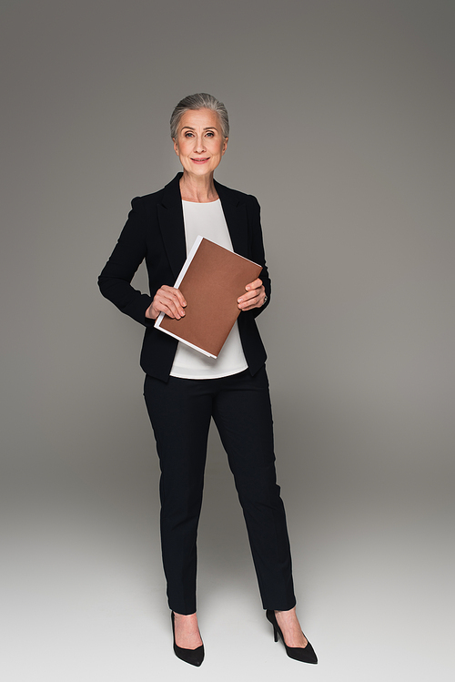 Mature businesswoman holding paper folder on grey background