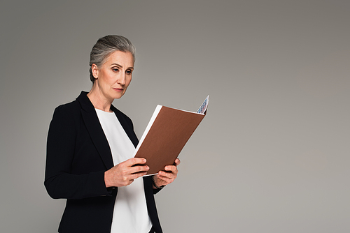 Middle aged woman in formal wear looking at paper folder isolated on grey