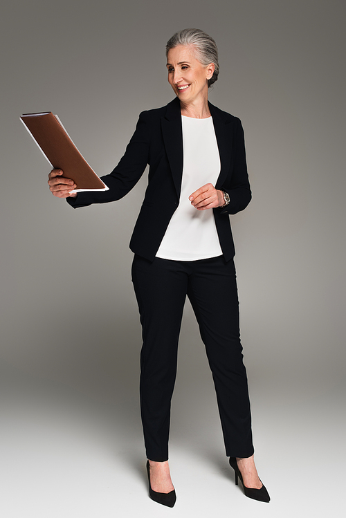 Smiling mature businesswoman looking at paper folder on grey background