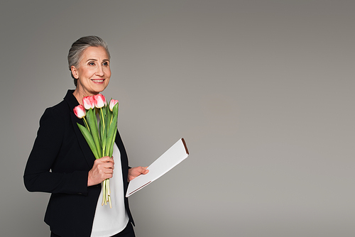 Smiling businesswoman holding paper folder and tulips isolated on grey