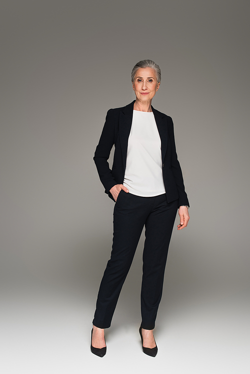 Middle aged businesswoman with hand in pocket  on grey background