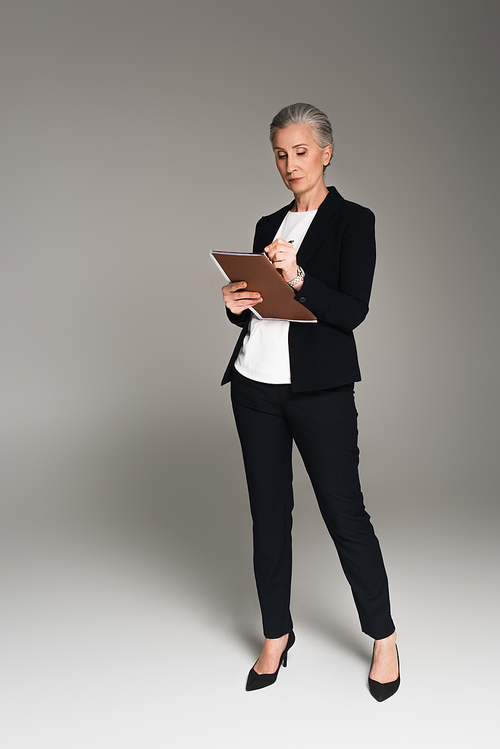 Businesswoman writing on paper folder on grey background