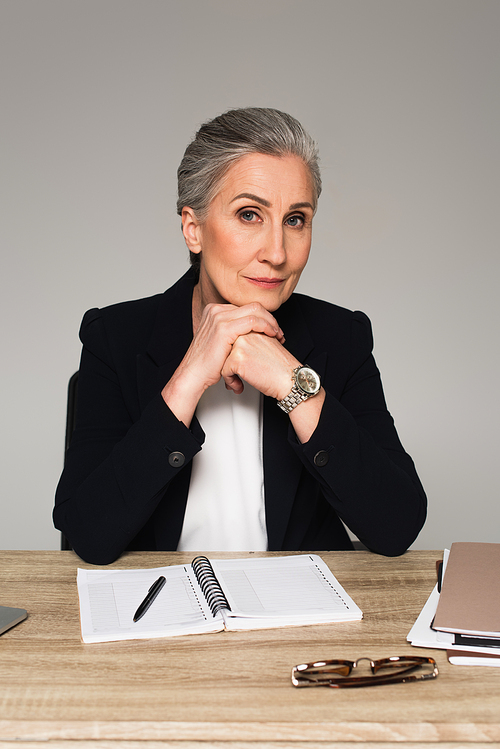 Mature businesswoman  near notebook and eyeglasses isolated on grey