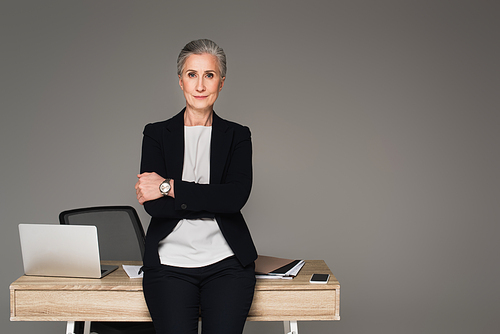 Businesswoman standing near gadgets and documents on table isolated on grey