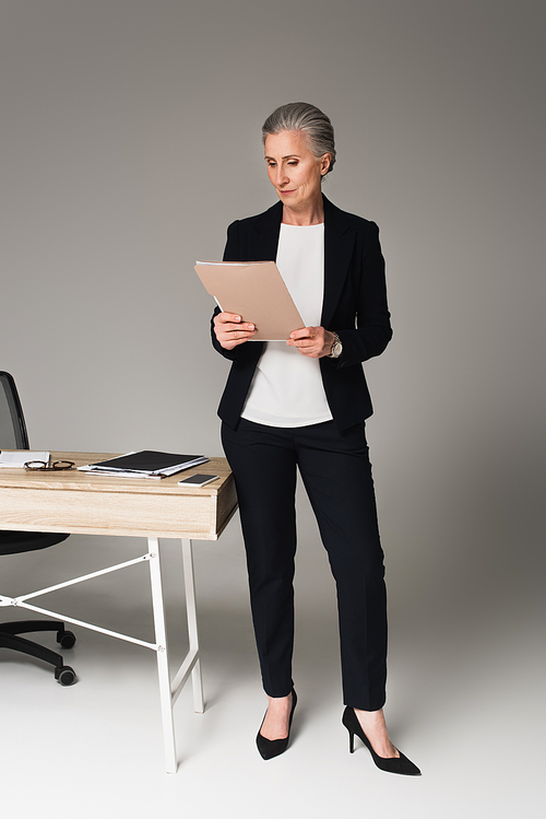 Businesswoman looking at documents near table on grey background