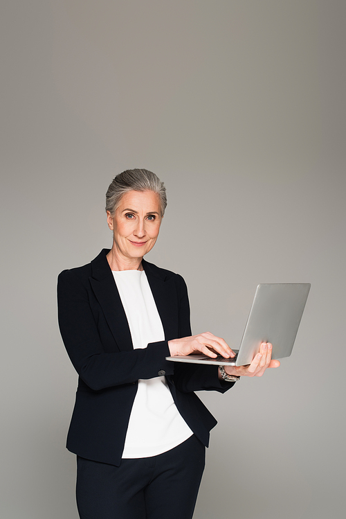 Mature businesswoman using laptop and  isolated on grey