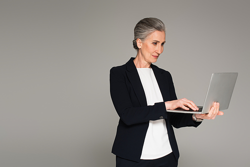 Businesswoman in formal wear using laptop isolated on grey