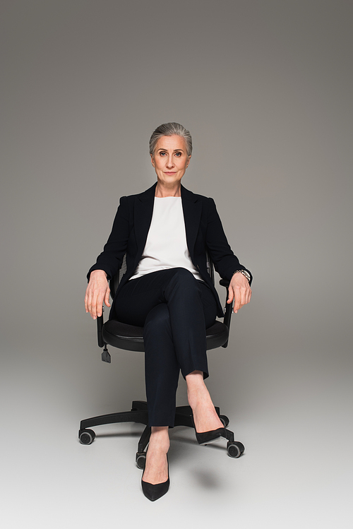 Mature businesswoman  on office chair on grey background
