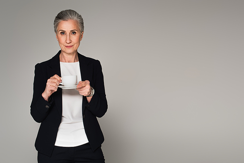 Grey haired businesswoman holding cup of coffee isolated on grey