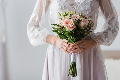 cropped view of bride in white dress with wedding bouquet