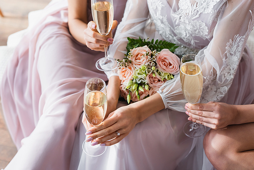 cropped view of bride and wedding bouquet near bridesmaids with champagne glasses