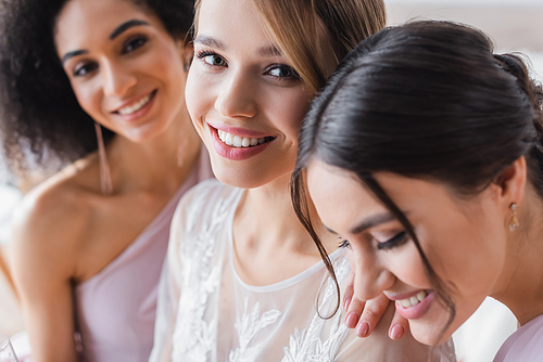 selective focus of young bride smiling at camera near interracial bridesmaids